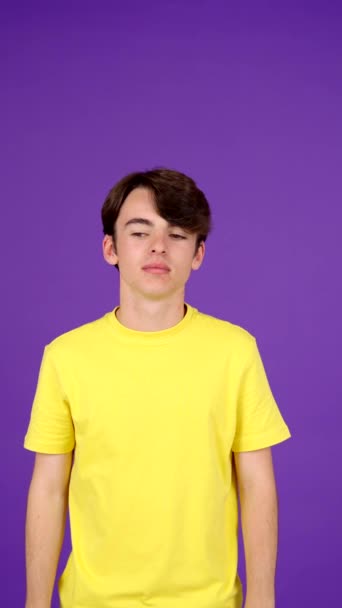 紫色の背景で隔離された脇の匂いを嗅ぐティーンエイジャーの少年 青少年問題コンセプト — ストック動画