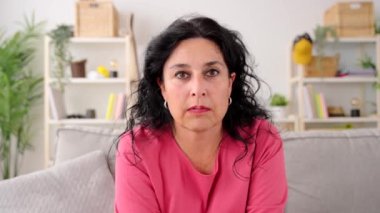 Orta yaşlı bir kadın evde video görüşmesi yapıyor. Kameraya bakıp konuşan biri.