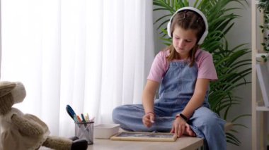 Pencerenin kenarına resim çizen küçük kız bir masanın üzerinde oturuyor. Hayal gücü konsepti