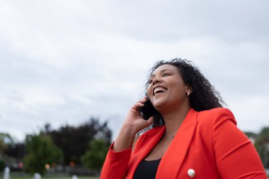 Siyah kıvrımlı pozitif kadın dışarıda telefonla konuşuyor. Afro-Amerikalı kişi kopyalama alanıyla gülümsüyor