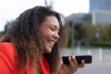 Dışarıdaki telefonda sesli mesaj gönderirken gülen siyahi kadın..