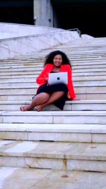 Pozitif siyah iş kadını dizüstü bilgisayarında video görüşmesi yapıyor. Afrikalı Amerikalı kadın merdivenlerde oturuyor..