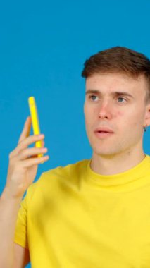 Genç adam telefonda konuşuyor. Telefon kullanan genç bir çocuk ve mavi arka planda izole edilmiş bir telefon..