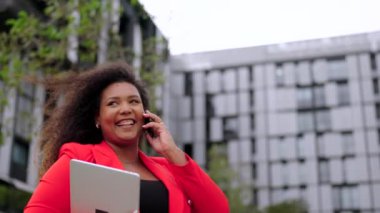Pozitif genç bayanın telefonda konuştuğu yakın plan. Ofis binalarıyla çevrili, kendine güvenen zenci bir iş kadını..