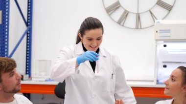 Laboratuvardaki iş arkadaşlarına test tüpünde numune gösteren genç bir bilim adamı.