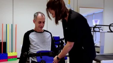 Bir hastayla ilgilenen hemşire. Fizyoterapist engelli bir adama dış iskelet giyiyor..