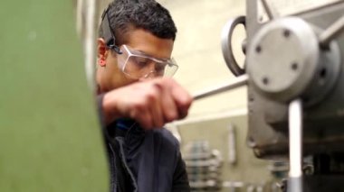 Koruyucu gözlüklü bir adamın CNC fabrikasındaki bir değirmen makinesini kullanışının videosu.