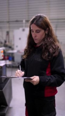 Modern bir fabrikada evrak işi yapan genç bir kadın mühendisin videosu. Sonra da kameraya gülümsüyor.