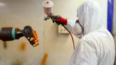 Çalışan, fabrikada sprey tabanca kullanan bir robot çiziyor..