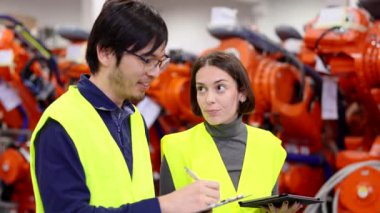 Fabrikada yürüyen ve konuşan pozitif iş arkadaşları. Mühendislik acemi çalışana depoda envanter çıkarmayı öğretiyor..