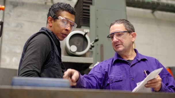 Cnc工場の若い労働者に機械の操作を説明する成熟したエンジニアのビデオ — ストック動画