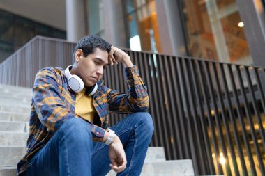 Endişeli genç adam dışarıda merdivenlerde oturuyor.