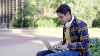 Kampüste dizüstü bilgisayar kullanan Latin bir öğrencinin yavaş çekimde yatay videosu.