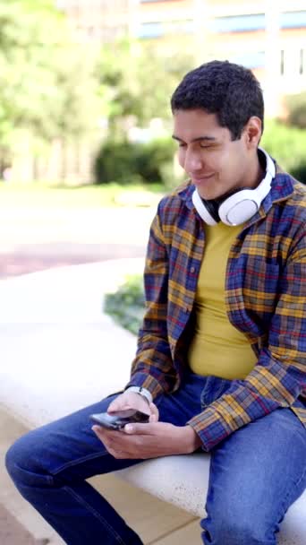キャンパスに座っている携帯電話を使用してラテン語の学生の垂直なスローモーションビデオ — ストック動画