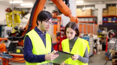 İki mühendis robot fabrikasında konuşuyor. Asyalı genç adam ve beyaz kadın belgeleri kontrol ediyor..