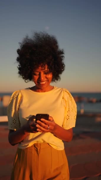 日落时一个微笑的女人在海边用电话拍下的录像 — 图库视频影像