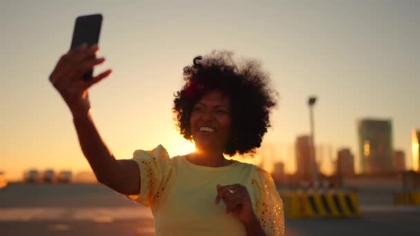 一个快乐的非洲女人在日落时站在城市里对着摄像机挥手的视频 — 图库视频影像