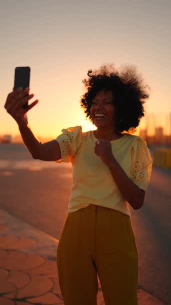一个快乐的非洲女人在日落时站在城市里对着摄像机挥手的视频 — 图库视频影像