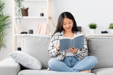 Kanepede kitap okuyan Çinli bir kadının ön görüntüsü.