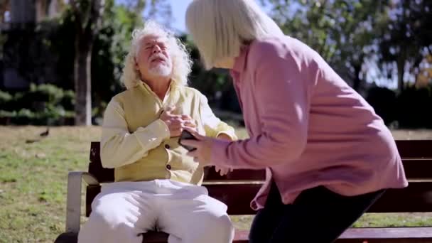 视频中 一位老年妇女坐在长椅上 一边喊着紧急呼救 一边男子心脏病发作 — 图库视频影像