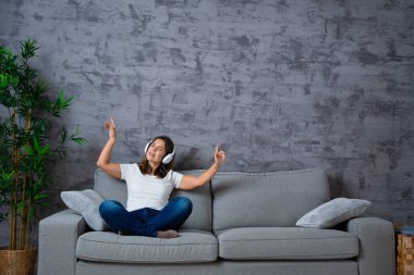 Kanepede oturmuş müzik dinlerken el kol hareketi yapan bir kadın.