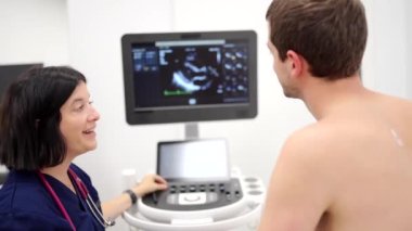Bir kadın kardiyolog ve genç bir erkek hastanın ekokardiyogram testi sırasında monitöre baktığı video.