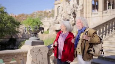 Güneşli bir günde iki yaşlı turistin şehir parkına şelaleyle ziyaretinin videosu.