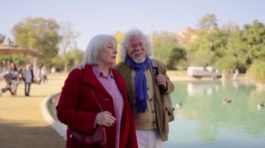 Yetişkin bir çiftin şehir parkında yapay bir havuzla sohbet edip yürümesini gösteren bir video.