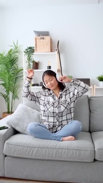亚洲年轻女子在耳机里听音乐 在沙发上休息的人 — 图库视频影像