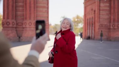 Yaşlı ve mutlu bir turist kadının şehirde fotoğraf çekerken poz verdiği bir video.