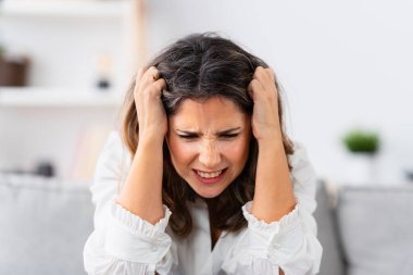 Kanepede oturan çaresiz bir kadın. Elleri başının üstünde evde oturuyor.