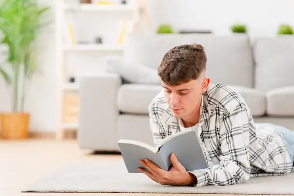 Young caucasian man studying lying on the floor. Person reading a book in the living room