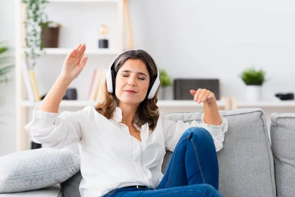 Woman closing eyes while enjoying music sitting on the sofa alone at home