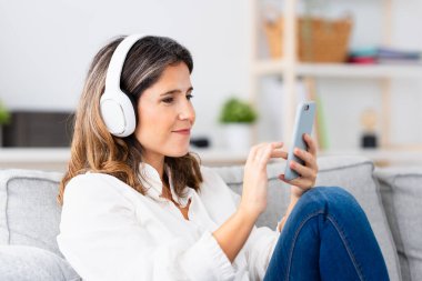 Evde telefon ve cep telefonu kullanarak müzik dinleyen modern olgun bir kadının yakın çekimi.