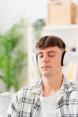 Genç adam, kulaklıkla, gözleri kapalı, rahatlatıcı müzik dinliyor.