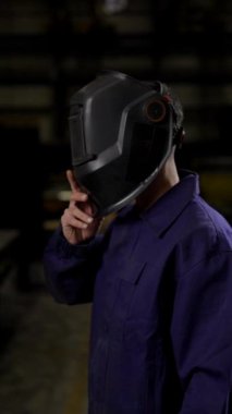 Kaynak işçisinin dramatik sinematik portresi koruyucu maskeyi çıkarıyor ve bir fabrikadaki kameraya bakıyor. Çalışma ve istihdam kavramı.