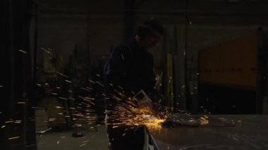 Karanlıkta metal kesen ve kıvılcım çıkaran bir işçi. Fabrikada çalışan işçilerin destansı sinema sahnesi..
