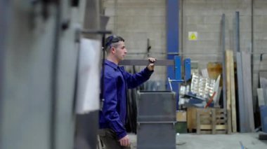 Omuzunda büyük bir kıskaç taşırken fabrikada yürüyen güçlü bir işçi..