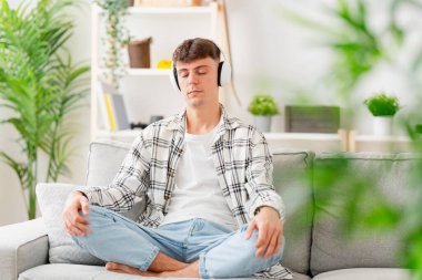 Genç çocuk müzik dinliyor ve dinleniyor. Genç adam kanepede meditasyon yapıyor..