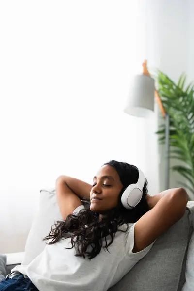 stock image Young Indian woman relaxing sitting on sofa with copy space. Teenager listening to music on headphones.