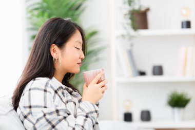 Çinli bir kadın evdeki kanepede oturan bir fincan kahvenin kokusunu alıyor.
