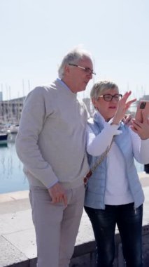 Üst düzey bir turist dışarıda video görüşmesi yapıyor. Limanda telefonla konuşan yaşlı bir adam ve kadın..