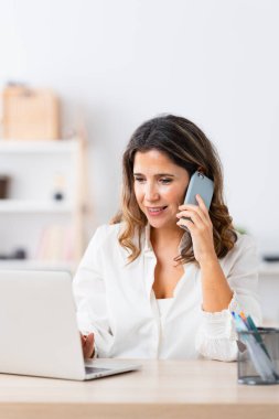 Evden uzakta bilgisayar ve telefon kullanarak çalışan olgun, zarif bir kadının dikey fotoğrafı.