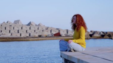 Genç kızıl saçlı kadın deniz kenarında meditasyon yapıyor..