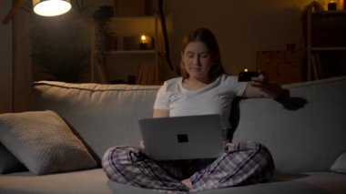 Genç bir kadın geceleri evdeki kanepede otururken internetten alışveriş yapıyor..