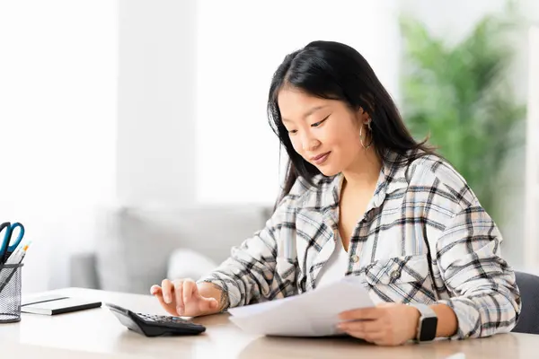 中国年轻女子坐在客厅里用计算器编制家庭预算 图库照片