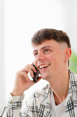 Evdeki cep telefonuyla konuşan yakışıklı bir gencin fotokopi çekilen dikey fotoğrafı.