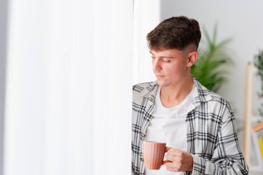 Pencereye bakıp kahve içen genç bir adamın sakin bir sahnesi.