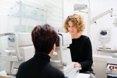 Bir hastayla çalışan kadın göz doktoru. Klinikte dijital otostraktometre kullanan bir oftalmolog..