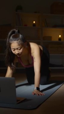 Genç Çinli bir kadın dizüstü bilgisayardan beden eğitimi dersini takip ediyor. Sporcu kadın geceleri evde antrenman yapıyor..
